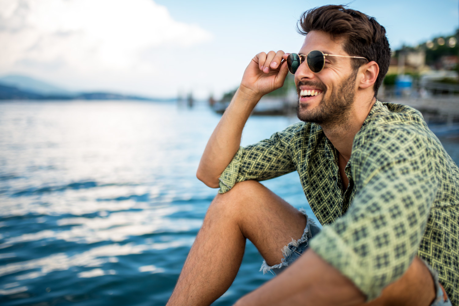 Brunette man wearing a green shirt and sunglasses smiles by a lake with healthier gums in Denver, CO