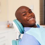Bald man with dental implants smiles while sitting in a dental chair at the dentist in Denver, CO