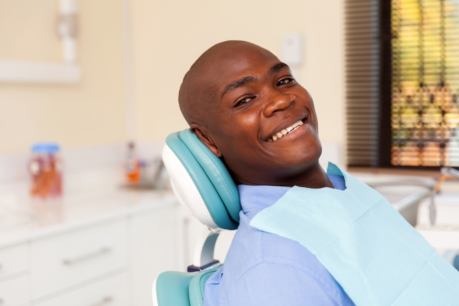 Bald man with dental implants smiles while sitting in a dental chair at the dentist in Denver, CO