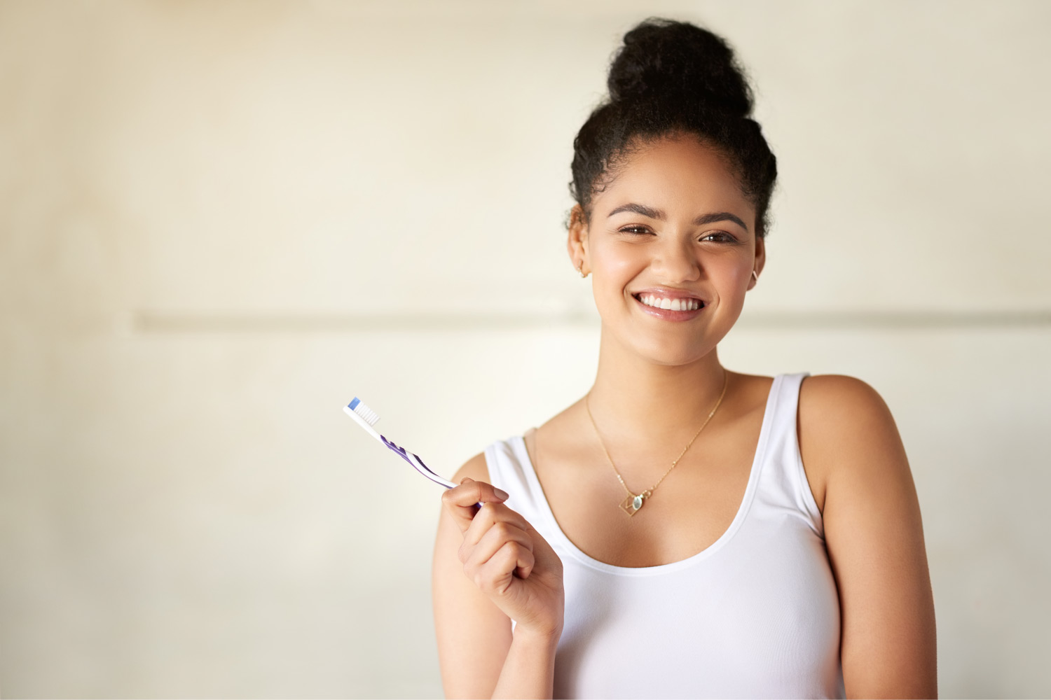 Brunette girl in a white tank top smiles while holding her toothbrush to care for her oral health