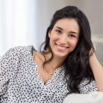 Brunette woman in a polka dot shirt smiles because she is a good candidate for dental implants in Denver, CO