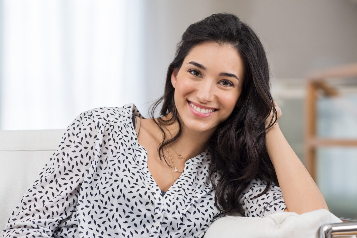 Brunette woman in a polka dot shirt smiles because she is a good candidate for dental implants in Denver, CO