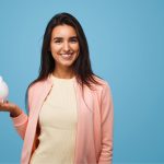 Brunette woman smiles as she holds a white piggy bank because she gets affordable dental care at Vero Dental in Denver, CO