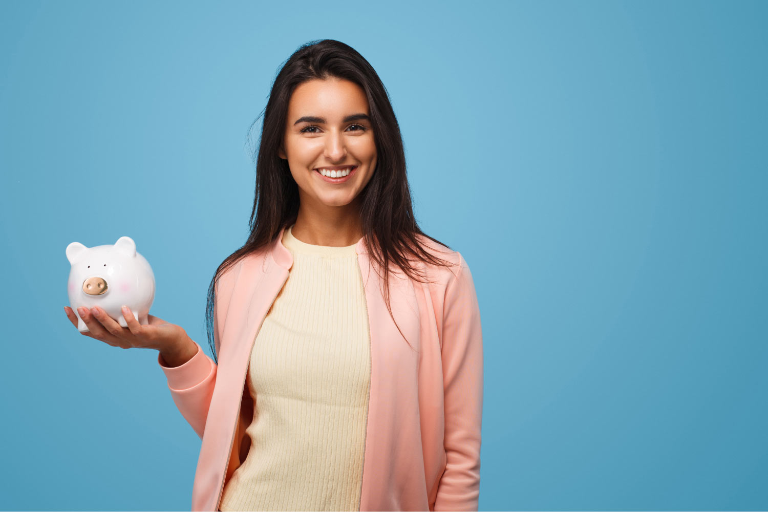 Brunette woman smiles as she holds a white piggy bank because she gets affordable dental care at Vero Dental in Denver, CO