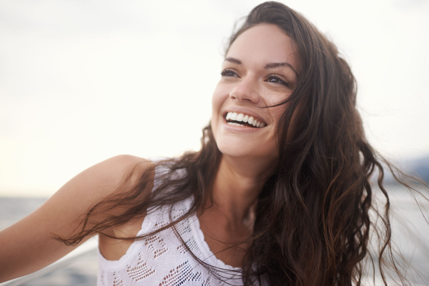 Brunette woman with permanent porcelain veneers smiles in Denver, CO