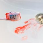 Closeup of a toothbrush with blood on it and blood in the sink from gum disease