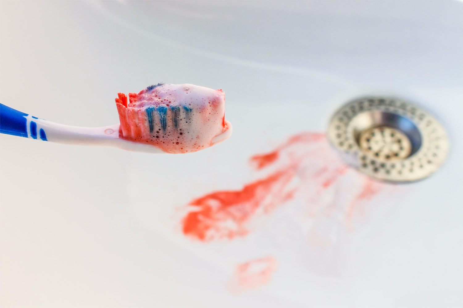 Closeup of a toothbrush with blood on it and blood in the sink from gum disease