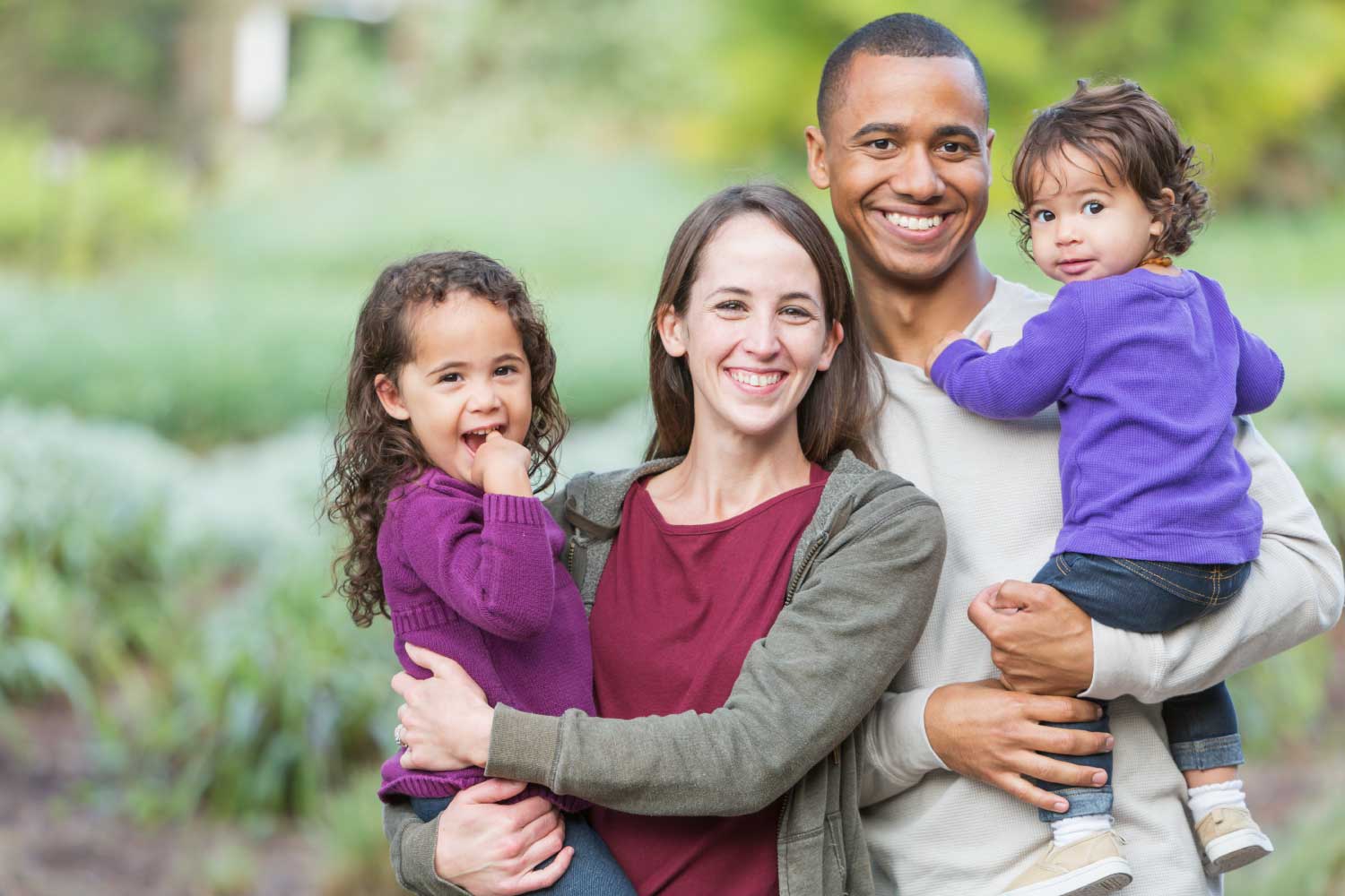 Mom and dad smile while holding their 2 daughters outside before going to their family dentist in Denver, CO