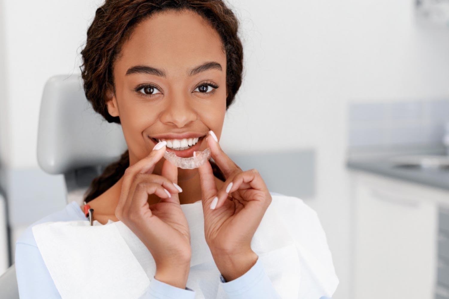 Pretty brown eyed girl holding a clear aligner in front of her smile.