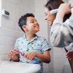Young boy smiles at his mom after brushing his teeth at the bathroom sink