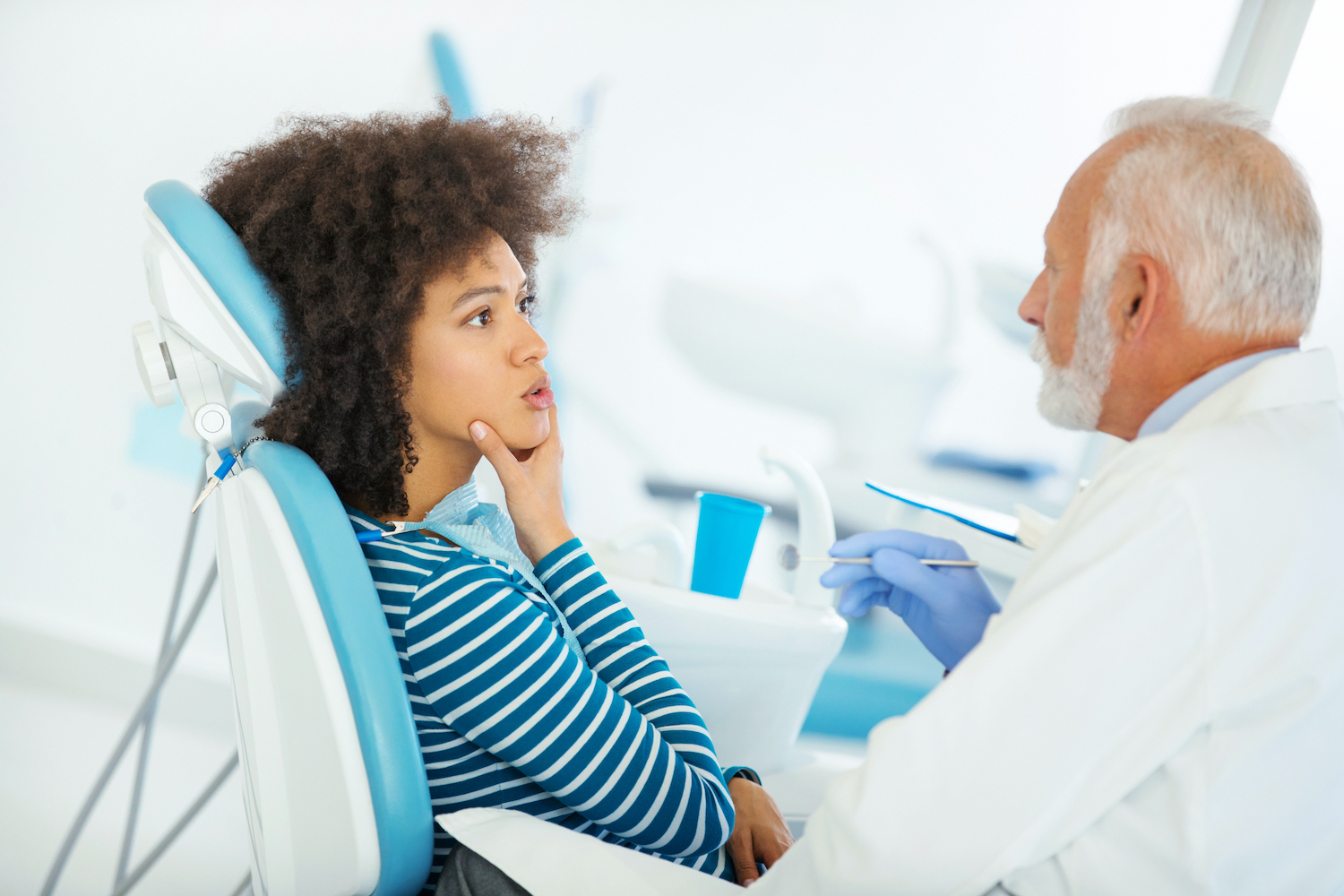 Black woman touches her face and talks to her dentist while sitting in a dental chair
