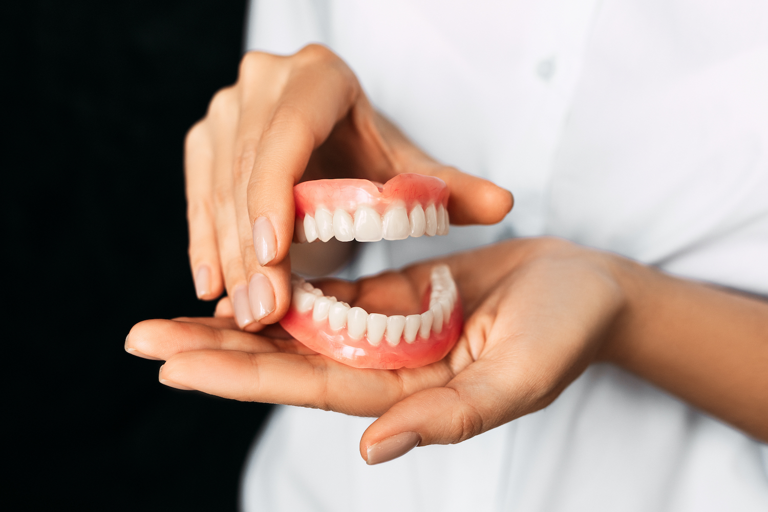 Closeup of hands holding full dentures to replace missing teeth