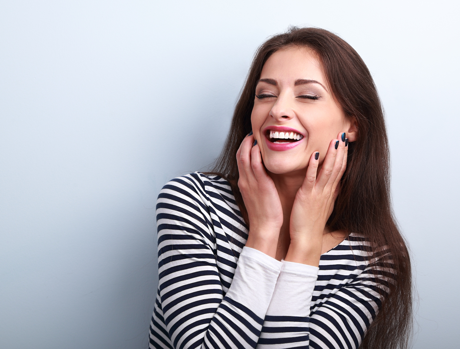 Brunette woman in a striped shirt smiles while touching the sides of her face