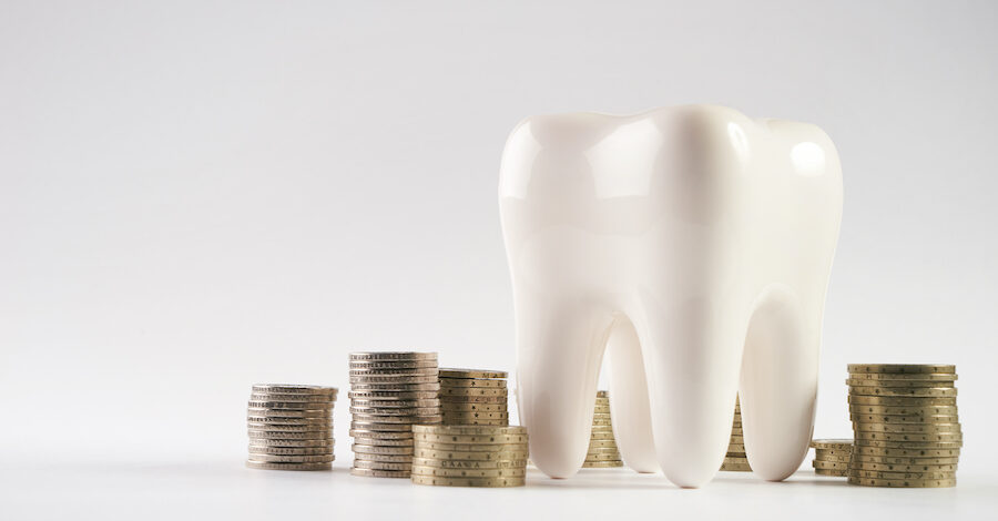 A white tooth next to several stacks of coins